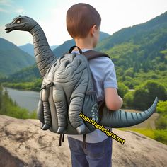 a young boy is carrying an inflatable dinosaur backpack on his back while looking at the mountains