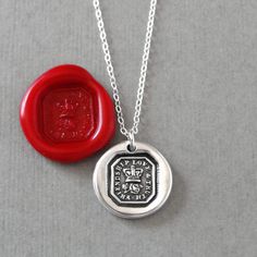 a wax seal necklace with a red wax stamp on the front and back of it