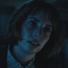 a woman with blue eyes stares into the distance in a dark room, wearing a suit and tie