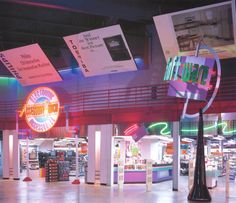 the inside of a grocery store with neon signs hanging from it's ceiling and advertisements on the walls