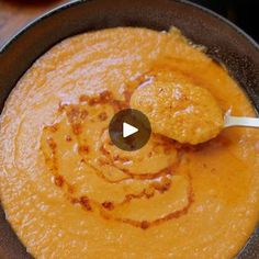 a bowl filled with orange colored soup and a spoon in the bowl next to it