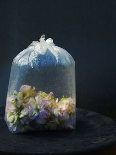 a plastic bag filled with flowers on top of a wooden table in front of a dark background