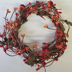 a wreath with red berries and green leaves hanging from it's sides on a white wall