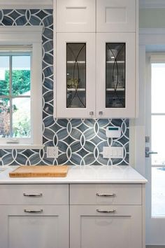 a kitchen with white cabinets and blue patterned backsplash