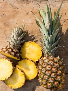 three pineapples on a wooden table with one cut in half