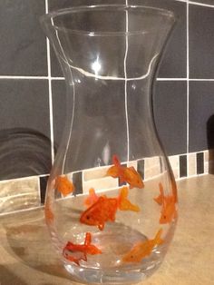 a glass vase filled with goldfish sitting on top of a counter next to a tiled wall