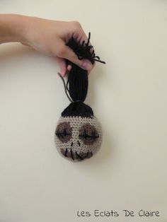 a hand holding a small crocheted skull ornament on a white surface