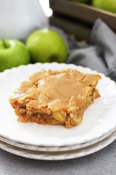 there is a piece of apple pie on the plate next to two green apples in the background