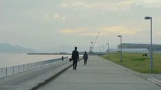 two people walking down a sidewalk next to the ocean