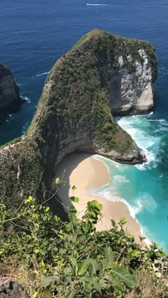 two large rocks sticking out of the ocean next to a sandy beach with blue water