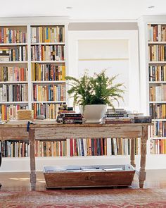 a room filled with lots of books and a wooden table in front of a window