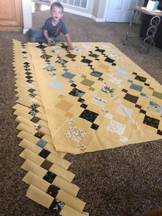 a young boy is sitting on the floor next to a large piece of quilting