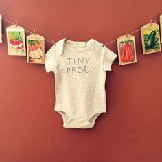 a baby's bodysuit hanging on a clothes line with tiny sprouts