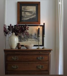 a wooden dresser topped with a white vase filled with flowers next to a framed painting