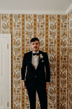 a man in a tuxedo standing next to a wall with gold and white designs