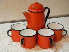 an orange tea pot and six cups on a doily