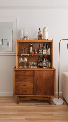 a wooden cabinet with wine glasses and liquor bottles on it's top, next to a white couch