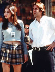 a man standing next to a woman in a plaid skirt and white shirt on the street