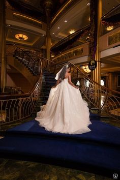 a woman in a wedding dress is standing on the blue carpeted stairs and looking down