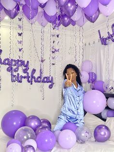 a woman sitting on top of a bed surrounded by purple and white balloons with the words happy birthday