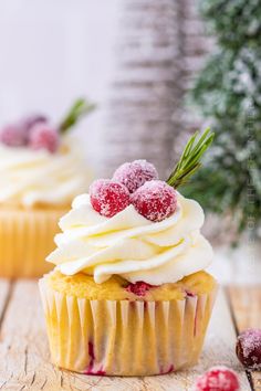 two cupcakes with white frosting and raspberries on top are sitting on a wooden table