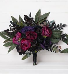 a bouquet of purple and black flowers on a white background with greenery in the center