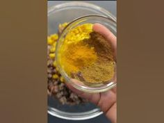 a hand holding a glass bowl filled with yellow and brown colored powdered food items