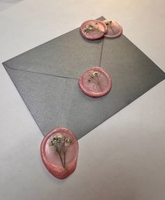 two pink buttons on top of an envelope with flowers in the middle and one button that has been pressed into it