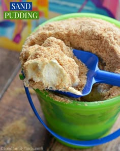 a scoopful of sand pudding is in a green bowl with a blue plastic spoon