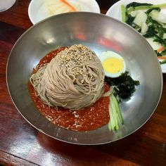 a plate with noodles, vegetables and eggs on it sitting on a wooden table next to other plates