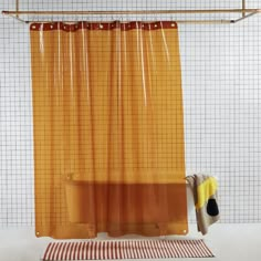 a yellow shower curtain hanging over a bathtub next to a rug and towel on a tiled floor