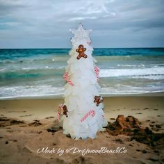 a plastic bottle christmas tree sitting on top of a sandy beach next to the ocean