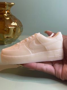 a hand holding a white nike air force shoe in front of a gold vase on a table