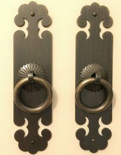 two metal door handles on the side of a white wall with an ornate design and round knobs