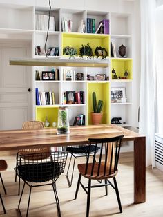 a dining room table and chairs in front of bookshelves with plants on them