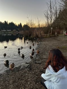 a woman sitting on the edge of a lake watching ducks