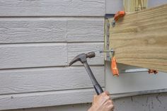 a man is holding a hammer in front of a siding board with nails on it