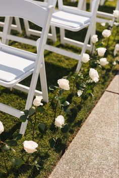 white chairs lined up in the grass with flowers