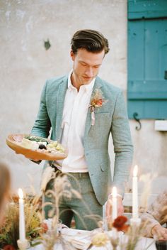 a man holding a plate with food on it in front of some candles and flowers