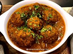 a white bowl filled with meatballs covered in gravy and garnished with parsley