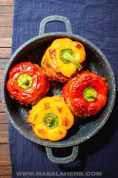 four stuffed peppers in a skillet on a blue towel next to a wooden table