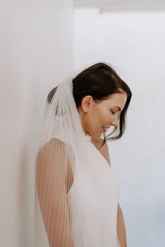 a woman in a white dress is wearing a veil and looking down at her hair