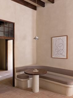 a corner table and bench in a room with beige walls, white tile flooring and wooden beams