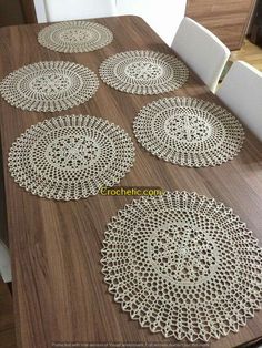 four crocheted doily on a wooden table with white chairs in the background