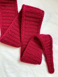 two crocheted red mittens and scarf laying on top of a white blanket