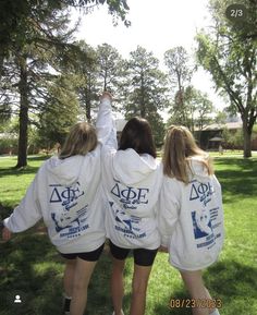 three girls in white sweatshirts holding hands up to the sky while standing on grass