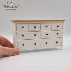 a hand holding a miniature white dresser with black knobs