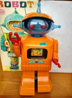 an orange robot toy sitting on top of a wooden floor