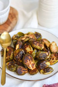 a white plate topped with brussel sprouts and a gold spoon next to it