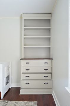 a baby crib in the corner of a room next to a bookcase and dresser